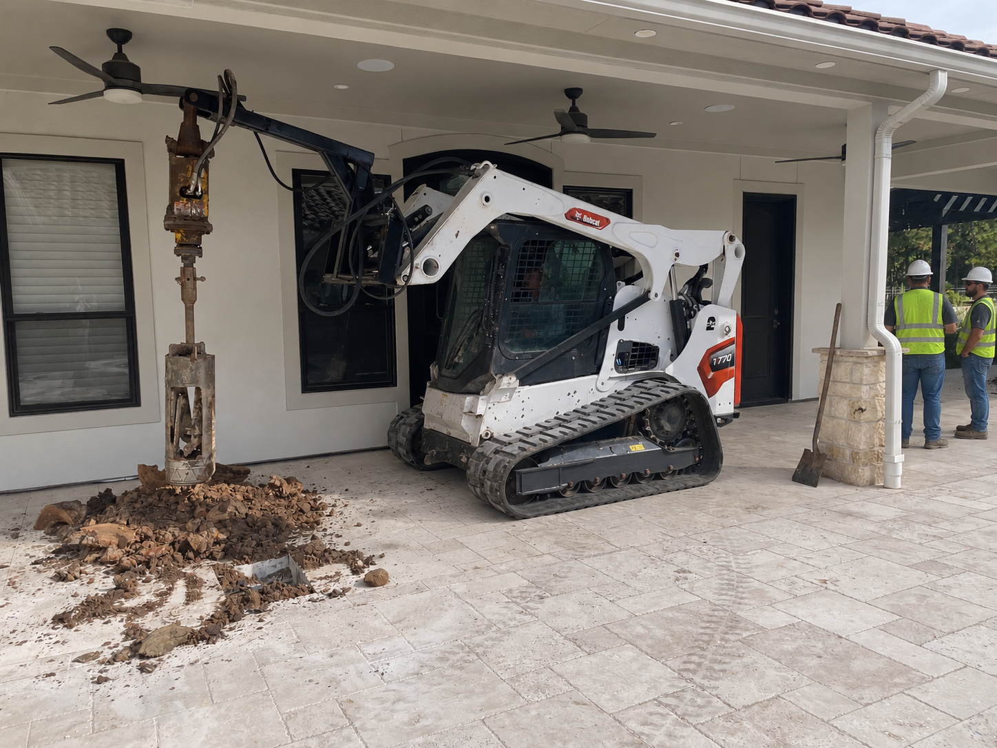Compact equipment drilling a pier under a covered patio