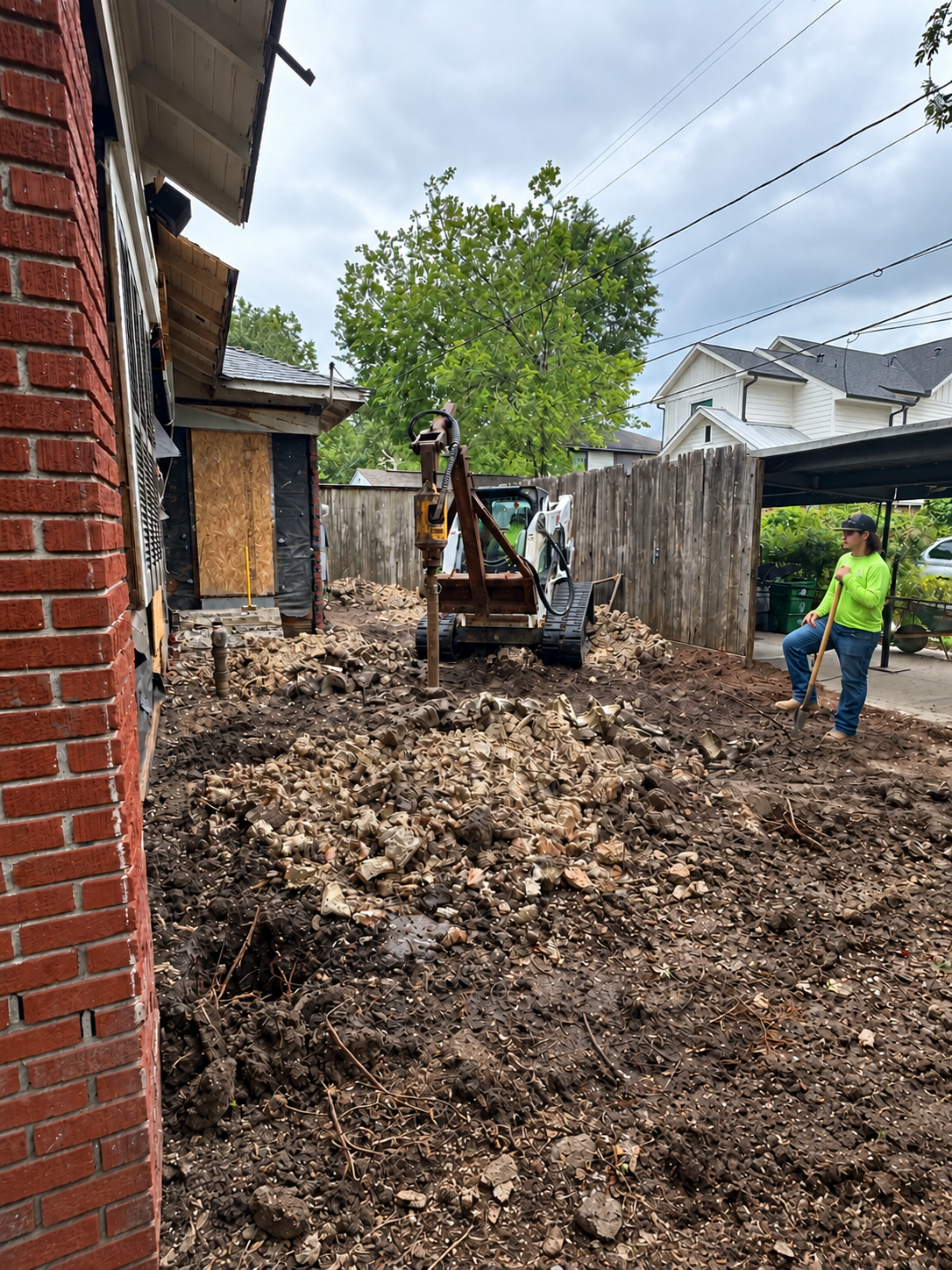 Compact equipment drilling in a narrow residential yard beside a brick wall